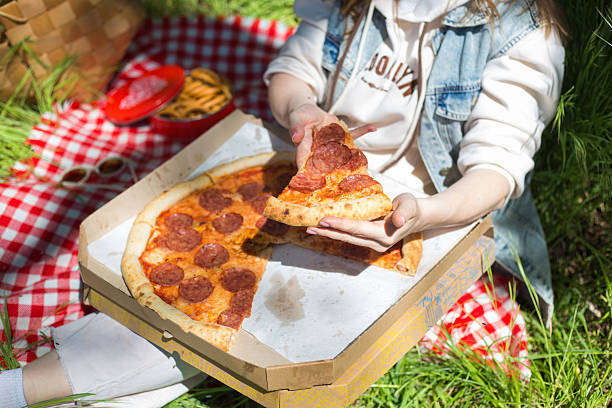 Woman eating pepperoni pizza during picnic on grass