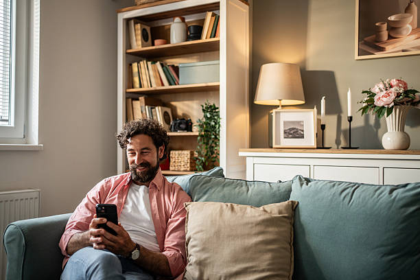 istock Smiling man relaxing on sofa using smartphone at home 2217697602