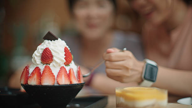 Asian mature woman and teenage girl enjoying dessert at cafe.