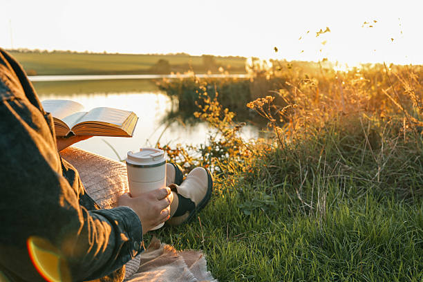 istock Girl by the river reading a book, beautiful sunset 2217703126