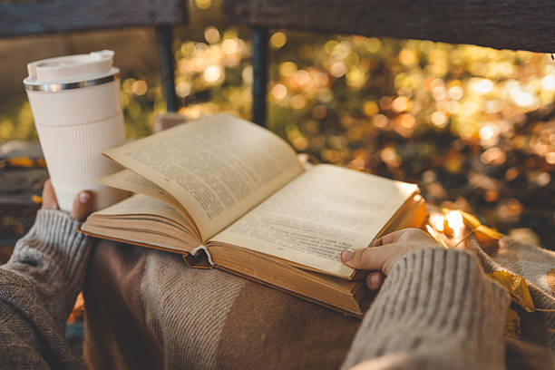 istock Person in cozy sweater holding reusable cup while reading a book outdoors in autumn park, surrounded by warm tones, fallen leaves, and soft sunlight 2217703177