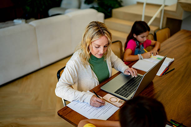 istock Mid adult woman working using laptop while kids drawing at home 2217711239