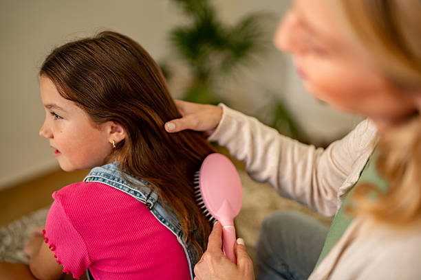 Mother combing daughter's hair on bed at home