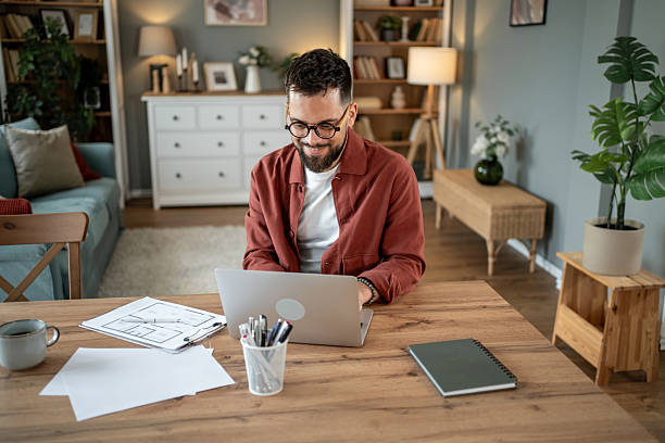 istock Architect working from home on laptop with blueprint plans 2217715665