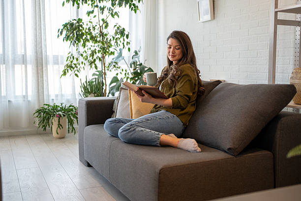 istock Young woman relaxing on sofa reading a book and drinking tea 2217715687
