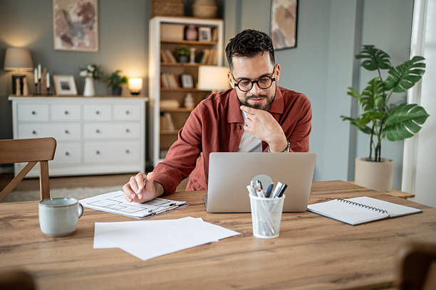 istock Focused architect working remotely on laptop with floor plans at home 2217715696