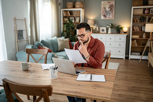 istock Focused freelancer reading documents and working on laptop at home 2217715719