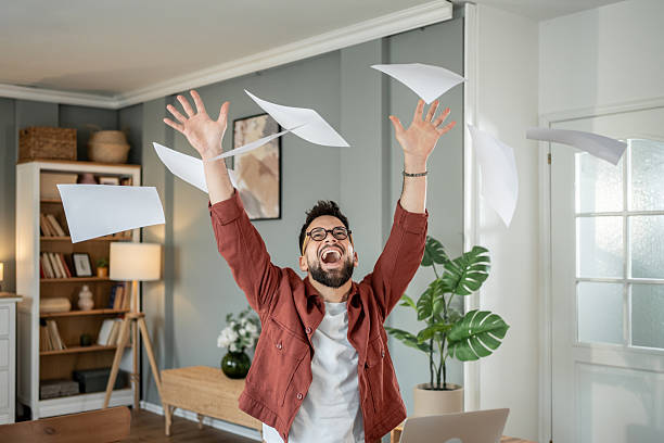 istock Happy young man throwing papers in the air celebrating success at home 2217715744