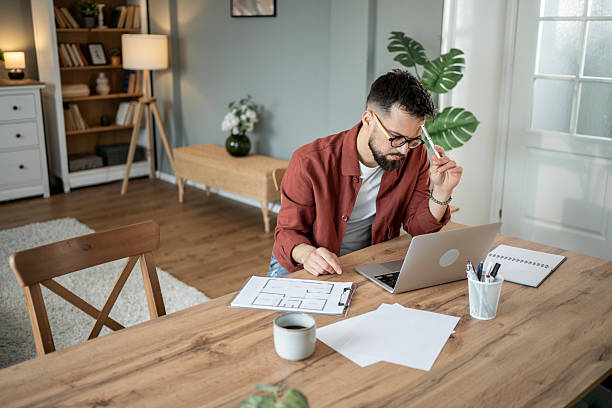 istock Focused architect working remotely from home on laptop with blueprint plans 2217715955