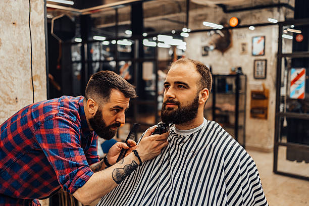 istock Barber trimming customer's beard in barbershop 2217718275