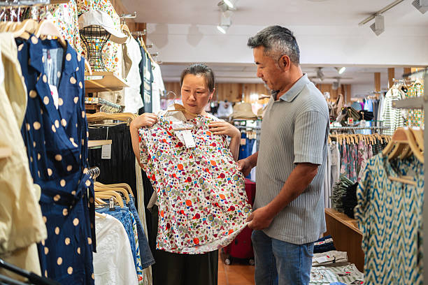 Mature couple browsing colorful clothing, smiling and selecting vibrant shirt during relaxed shopping trip together Happy mature couple examining a vibrant shirt while enjoying a leisurely shopping experience together in a clothing store colorful check shirts on sale at a clothing store stock pictures, royalty-free photos & images