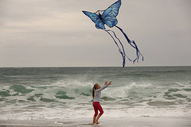 Young girl running along beach chasing the tail of a butterfly shaped kite