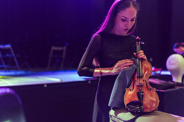 istock Woman attentively cleans her violin using a cloth. Her intent expression shows the care and attention given to maintaining the instrument in perfect condition 2217726371