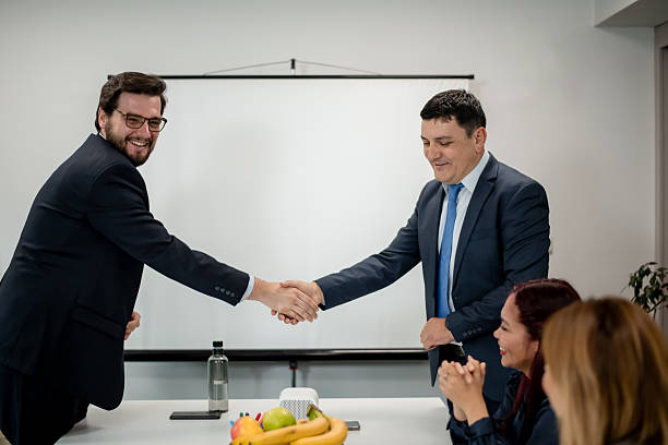 istock Business professionals shaking hands in an office environment with colleagues observing and a presentation screen in the background 2217726593