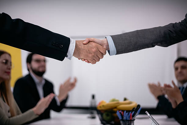 istock Two professionals sealing a business deal with a handshake while colleagues applaud during a meeting 2217726636
