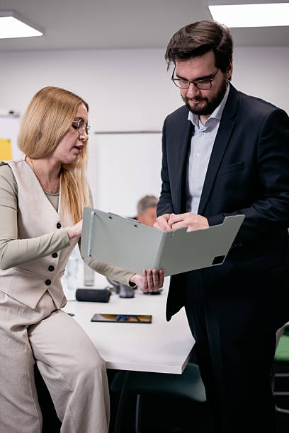 istock Two professionals in formal attire collaborating on documents in a modern office setting with a focused environment. 2217726695