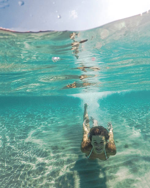 Young woman swimming in the swimming pool under the water, towards camera. Underwater photoshoot, active vacation lifestyle