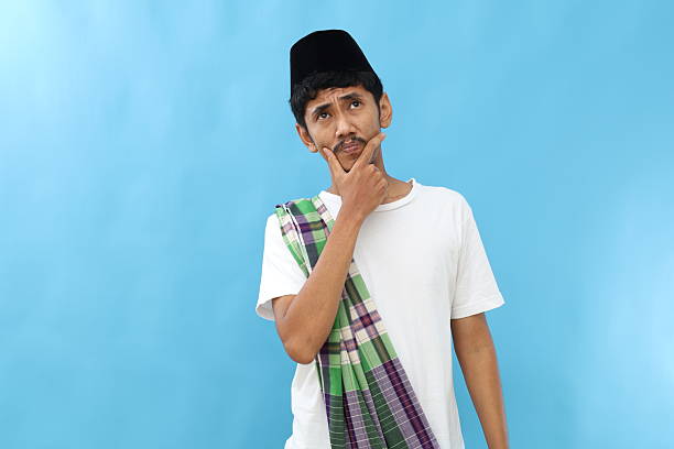 Thoughtful asian muslim man standing while thinking an ideas. Isolated on blue background