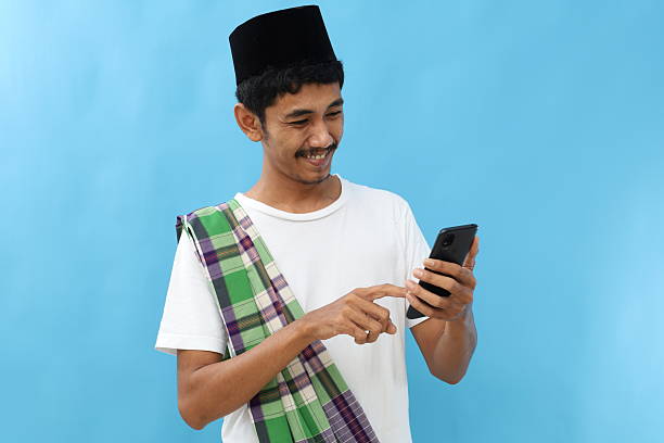 istock Portrait of asian muslim man standing while using cell phone. Isolated on blue 2217737968