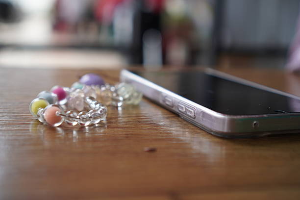 A contemporary smartphone lies beside a vibrant, handcrafted beaded bracelet on a textured wooden table, representing a blend of modern connectivity and personal expression. This image is suitable for editorial narratives exploring daily rituals, personal technology, digital detox, or the intersection of modern life and handcrafted aesthetics. Evokes a sense of quiet downtime