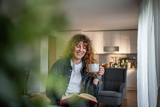 istock Young woman reading a book and drinking coffee at home 2217748018
