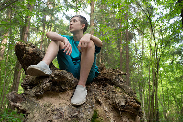 istock A pensive 12 year old boy sits on a snag in a summer forest, looking away. 2217751899