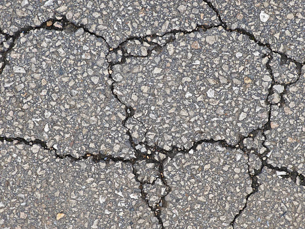istock Cracked asphalt surface with varying textures and stones visible during daylight in an urban area 2217753635