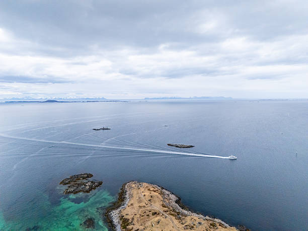 Aerial view of a boat navigating along the rugged Norwegian coastline. Stunning seascape with rocky islands. Ideal for showcasing Norway's natural beauty and coastal adventures.