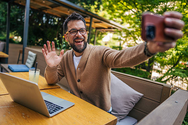 istock Young man video calling and waving at outdoor cafe 2217759028
