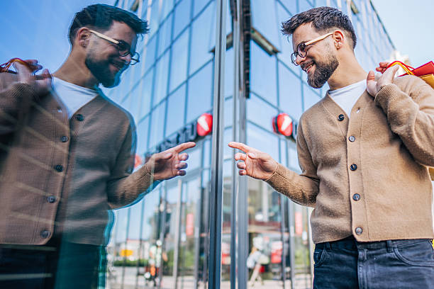 Young man touching his reflection in a modern building's glass window