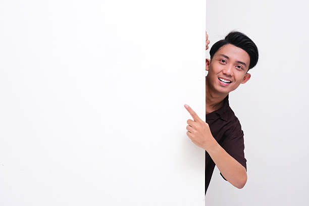 istock Young Asian man peeking from behind blank wall with happy face 2217761051
