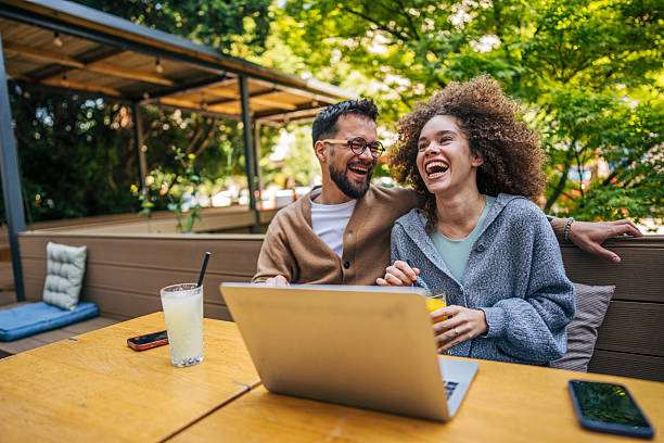istock Young couple laughing while watching something on laptop in outdoor cafe 2217761400