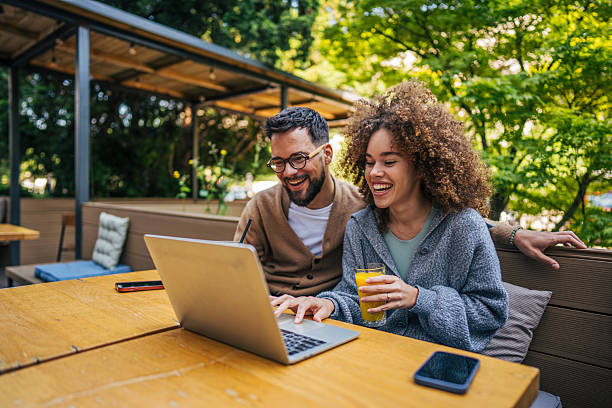 istock Young couple laughing and using laptop at outdoor cafe 2217761423