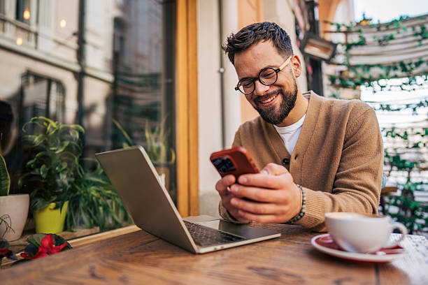 Freelancer smiling and using smartphone in outdoor cafe