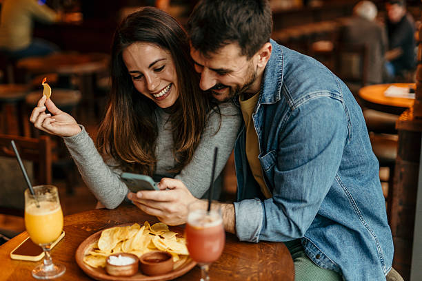 istock Happy couple using smartphone and eating nachos in restaurant 2217763862