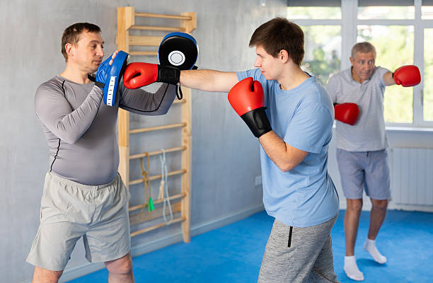istock Boxing training - young guy masters boxing strikes on trainer punch mitts during training 2217764335