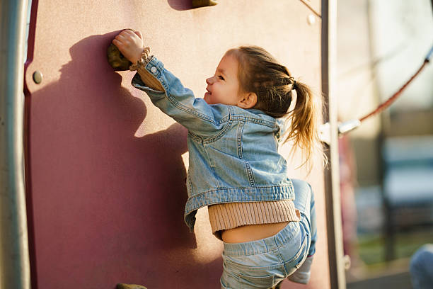 A cute little girl plays in the playground, hanging like a salami from the bars of an exercise ladder. You can tell from her eyes that she is in a bit of a predicament.