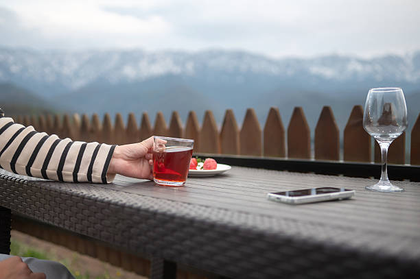 A hand grasping a drink on a textured table, with a breathtaking mountain landscape visible in the background, capturing a refreshing moment that signifies relaxation and enjoyment of nature.