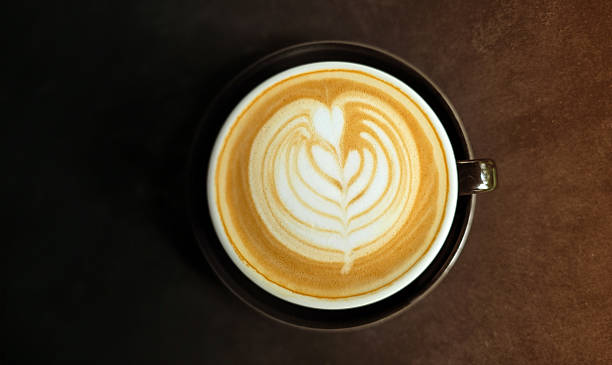 Cup of latte coffee with heart-shaped latte art on dark velvet background, top view