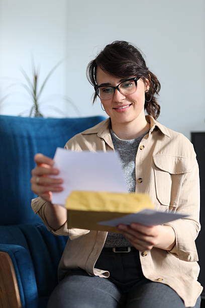 istock Young caucasian female smiling while opening mail in living room 2217769285