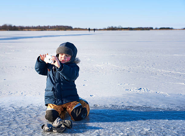 istock A young child explores curiosity and play on a frozen lake, kneeling in snow while using a toy camera. The clear sky and vast icy landscape highlight themes of wonder, discovery, and solitude 2217775620
