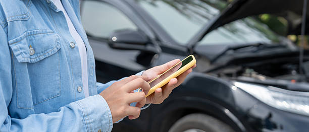 istock breakdown, broken car, repair. Woman uses mobile phone check insurance premiums through application due to car accident . Find garage to get car fixed during country tour, waiting for help, emergency. 2217779909