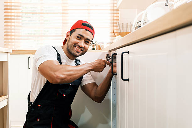 istock Smiling handyman fixing kitchen cabinet hinges, representing reliable home repair services, maintenance professionalism, and skilled craftsmanship in residential plumbing and handyman business. 2217781770
