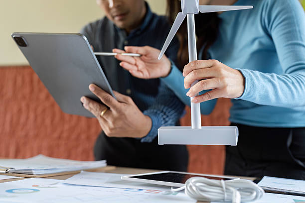 istock Sustainability Discussion. Professionals collaborating on renewable energy project with wind turbine model. 2217788126