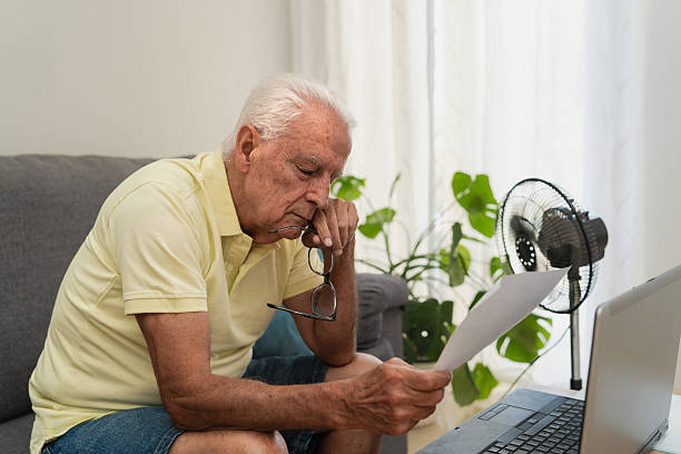istock Senior man worried about bills, checking invoice at home using laptop and refreshing with a fan 2217793970
