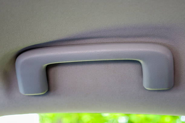 istock A close-up of a car interior, clearly showing a gray grab handle mounted on the light-colored ceiling lining. The bottom part of the image shows a blurred green background, indicating the exterior. 2217794246