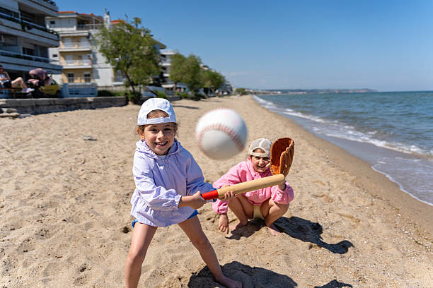Two young children are joyfully playing baseball on a sunny day at a sandy beach, highlighting the fun and active nature of their leisure activity in this serene coastal setting. Peraia,  Greece