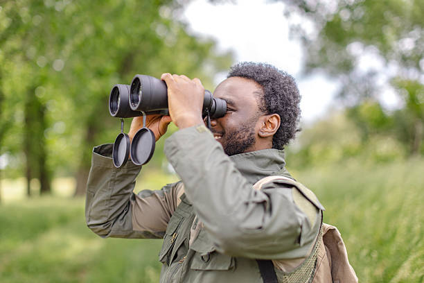 istock Curious young man enjoying birding with binoculars in a lush green forest on a sunny weekend adventure 2217806484