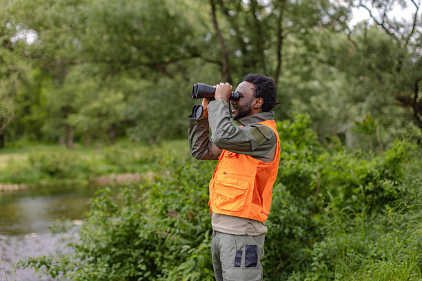istock Young man bird watching with binoculars in a lush outdoor environment surrounded by greenery 2217808944