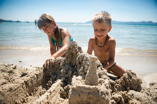 istock Two little kids playing on the beach, building a magnificent sandcastle 2217809350